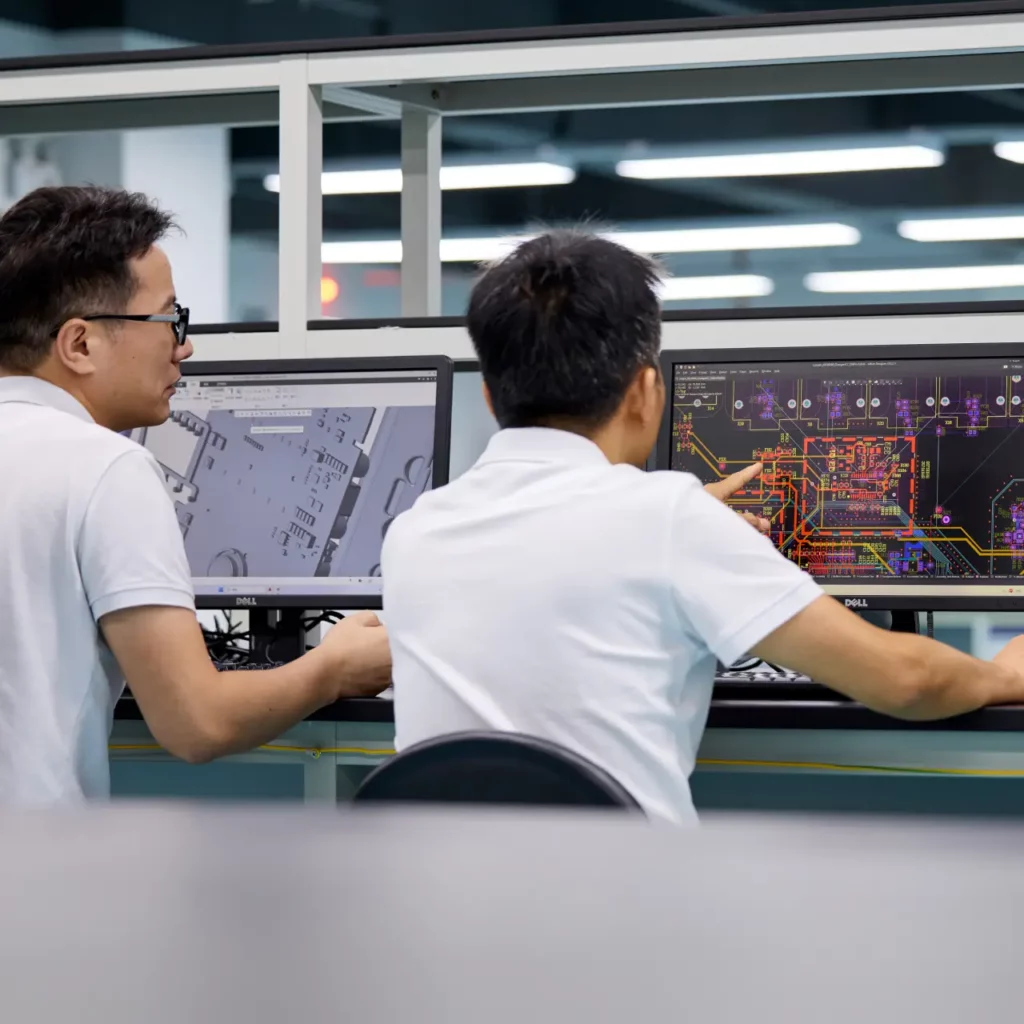 Two Ryder Industries engineers reviewing PCB layout design on monitors in a lab.