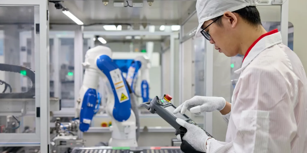 A Ryder Industries engineer in a white lab coat and cap directing a robotic arm.